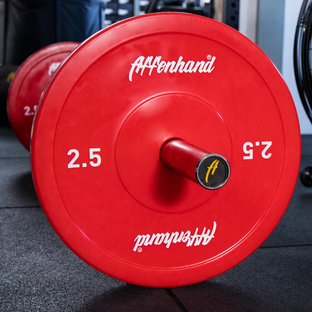 Rote Affenhand Technik Gewichtsscheiben mit 2,5 kg Aufdruck auf einer Langhantel, liegend auf dem Boden eines Trainingsraums.
